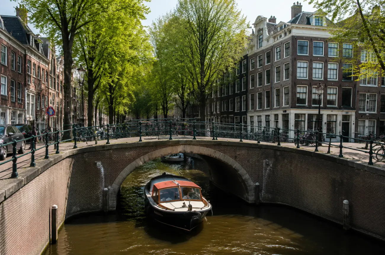 Amsterdam kanalında kemerli tuğla köprünün altından geçen üstü kapalı tur teknesi