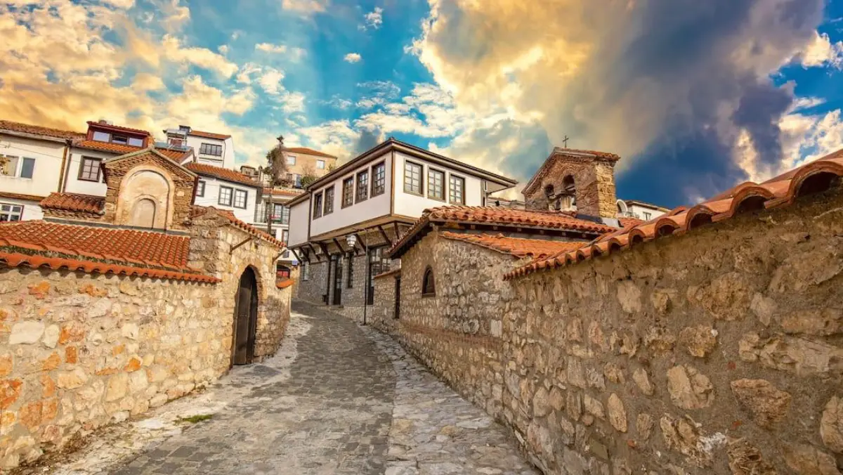 Ohrid eski şehrinde taş döşeli dar sokak, ahşap cumbalı evler ve küçük bir Bizans kilisesi